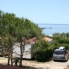 Vista su una casa mobile tra alberi e auto, con mare sullo sfondo.
