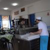 Interno di un ristorante con tavoli apparecchiati e cuoco al lavoro.