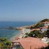 Case vicino a una spiaggia rocciosa con ombrelloni e mare calmo.