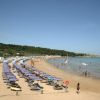 Spiaggia affollata con lettini e ombrelloni colorati, bagnanti in acqua.