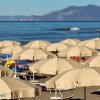 Spiaggia con ombrelloni beige aperti e mare sullo sfondo.