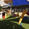 Un'area giochi per bambini con casetta, scivolo colorato e tunnel su erba sintetica.