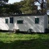 Una casa mobile bianca con finestre verdi, circondata da erba e alberi.
