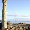 Rovine di una colonna davanti a un paesaggio marino con isole in lontananza.