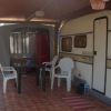 Caravan e area esterna coperta con sedie bianche e tavolo su pavimento piastrellato.