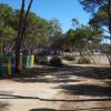 Strada sterrata tra alberi, con un parco giochi a sinistra e un parcheggio in lontananza.