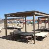 Pagode di legno e lettini su una spiaggia sabbiosa con case colorate sullo sfondo.