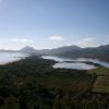 Una costa vista dall'alto, con mare, montagne e piante lungo la riva.