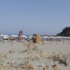 Spiaggia sabbiosa con ombrelloni e roccia collinare sullo sfondo.