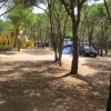 Area campeggio con una tenda blu, un'auto e un edificio giallo tra gli alberi.