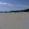 Spiaggia sabbiosa con mare in lontananza e alcune persone.