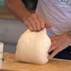 Mani impastano una grande quantità di pasta su un tavolo di legno.