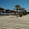 Passeggiata in legno sulla spiaggia con ombrelloni di paglia.