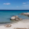 Spiaggia con sabbia bianca e rocce sul mare azzurro.