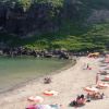 Spiaggia con ombrelloni rossi e bianchi, persone rilassate vicino ad una collina verde.