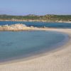 Spiaggia sabbiosa con mare azzurro e scogliere in lontananza.