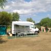 Camper bianco parcheggiato, con tenda e sedie all'aperto, alberi sullo sfondo.