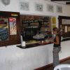 Donna prepara bevande al bancone di un bar con mensole di bottiglie dietro.