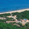 Veduta aerea di un complesso vicino a una spiaggia con acqua blu e una zona verde attorno.