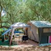 Tenda da campeggio sotto gli alberi, con sedie e tavolo all'esterno.
