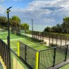 Un campo da padel verde circondato da recinzioni e alberi con vista sul mare.