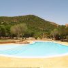 Piscina all'aperto con bordo di piastrelle, circondata da alberi e colline.
