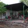 Patio coperto con tavolo e sedie, accanto a una roulotte tra gli alberi.