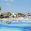 Piscina blu con lettini e ombrelloni bianchi e blu. Alberi e tende sullo sfondo.